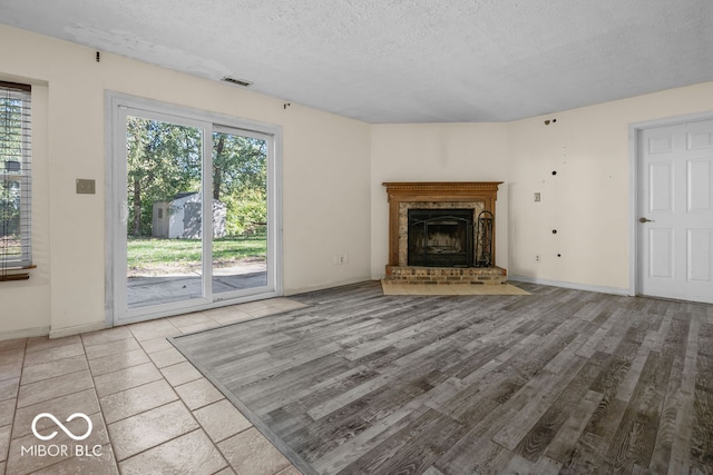 unfurnished living room with a brick fireplace, hardwood / wood-style floors, a textured ceiling, and a healthy amount of sunlight