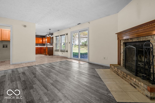 unfurnished living room with a notable chandelier, a brick fireplace, a textured ceiling, and hardwood / wood-style flooring