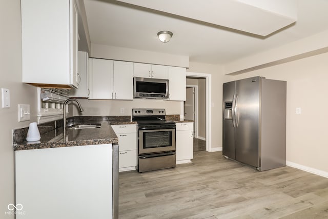 kitchen with white cabinets, sink, light hardwood / wood-style flooring, dark stone countertops, and stainless steel appliances