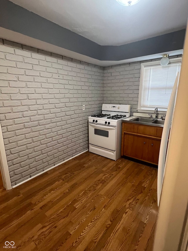 kitchen featuring brick wall, white gas stove, sink, and dark wood-type flooring