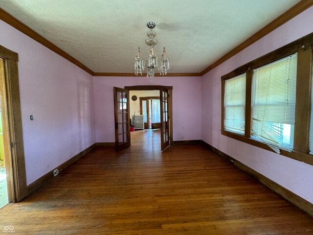 unfurnished dining area featuring french doors, a notable chandelier, hardwood / wood-style floors, and a textured ceiling