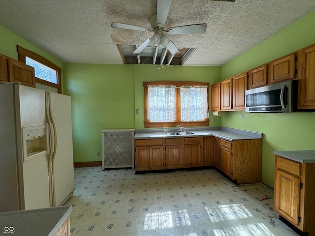 kitchen featuring a textured ceiling, white fridge with ice dispenser, ceiling fan, and sink