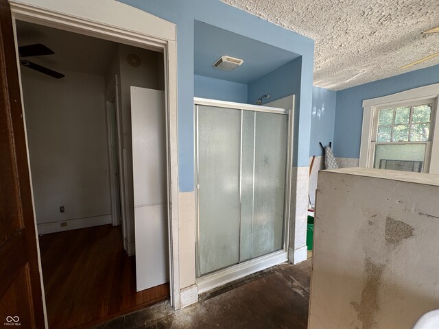 bathroom with a textured ceiling, wood-type flooring, ceiling fan, and a shower with shower door