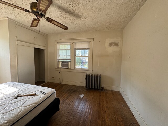 unfurnished bedroom featuring ceiling fan, cooling unit, radiator heating unit, a textured ceiling, and dark hardwood / wood-style flooring