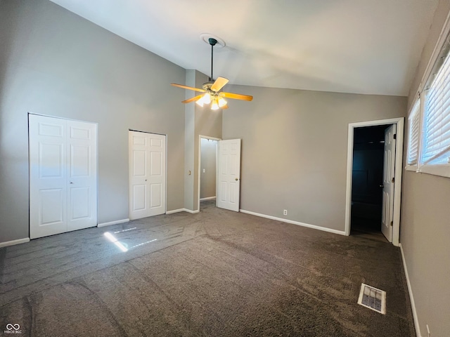 unfurnished bedroom featuring ceiling fan, two closets, dark colored carpet, and high vaulted ceiling