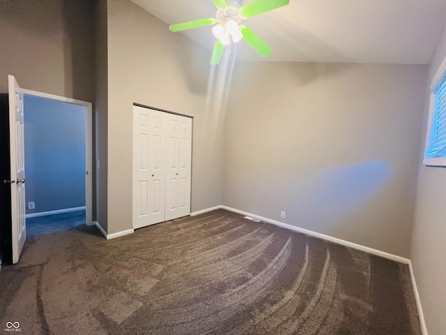 unfurnished bedroom with dark carpet, a closet, ceiling fan, and high vaulted ceiling