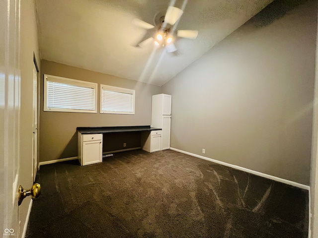 unfurnished bedroom with dark carpet, built in desk, vaulted ceiling, and ceiling fan