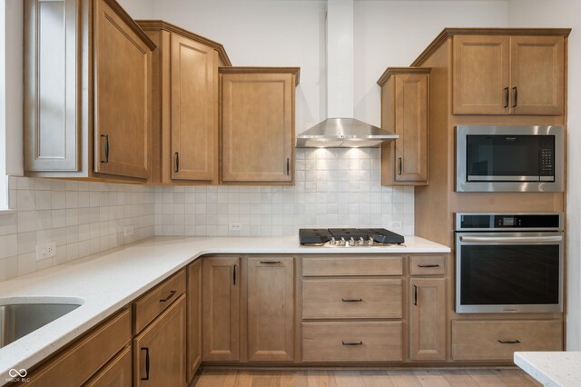 kitchen featuring tasteful backsplash, light hardwood / wood-style flooring, stainless steel appliances, light stone countertops, and wall chimney range hood