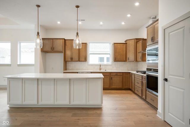 kitchen with light hardwood / wood-style flooring, appliances with stainless steel finishes, a kitchen island, pendant lighting, and backsplash