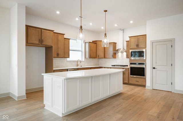 kitchen featuring a kitchen island, decorative light fixtures, sink, stainless steel appliances, and wall chimney range hood