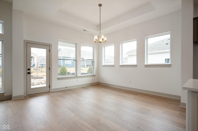 unfurnished dining area featuring an inviting chandelier, a tray ceiling, and light hardwood / wood-style flooring