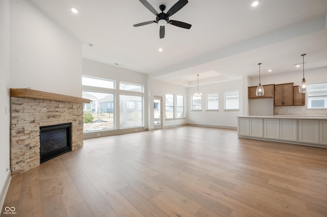 unfurnished living room featuring ceiling fan, a stone fireplace, a raised ceiling, and light hardwood / wood-style flooring