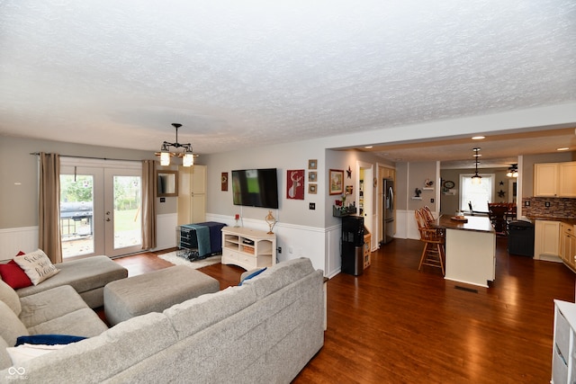 living room featuring dark hardwood / wood-style floors, a textured ceiling, an inviting chandelier, and french doors