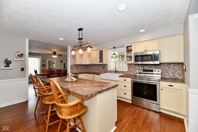 kitchen with sink, a breakfast bar, stainless steel appliances, decorative light fixtures, and cream cabinetry