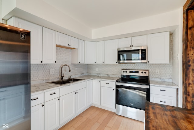 kitchen featuring light stone countertops, sink, appliances with stainless steel finishes, and light hardwood / wood-style flooring