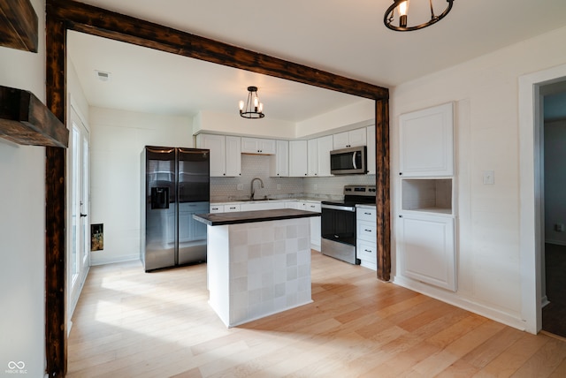 kitchen featuring hanging light fixtures, stainless steel appliances, a center island, light wood-type flooring, and white cabinets