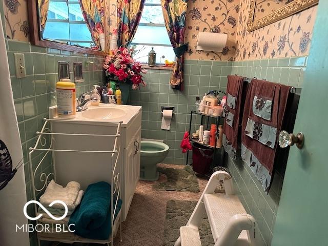 4434 E 46th St, Indianapolis, IN 46226 - bathroom with wallpapered walls, a wainscoted wall, toilet, vanity, and tile walls