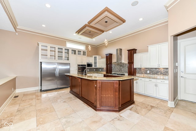 kitchen with ornamental molding, a center island with sink, wall chimney range hood, built in appliances, and decorative backsplash