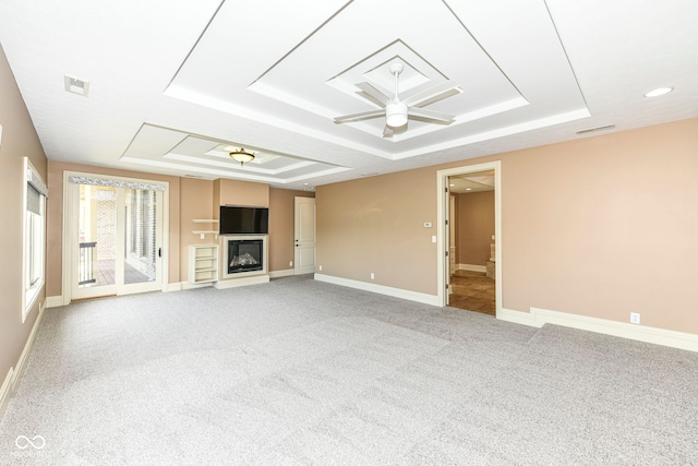 unfurnished living room featuring a raised ceiling, carpet flooring, and ceiling fan