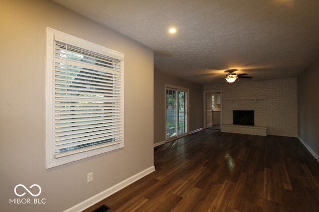 unfurnished living room with a brick fireplace, dark hardwood / wood-style floors, a textured ceiling, and ceiling fan