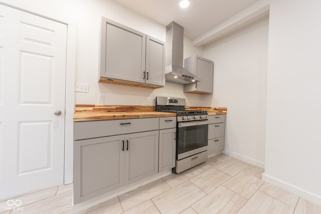 kitchen with gray cabinets, stainless steel gas range, wall chimney range hood, and wood counters