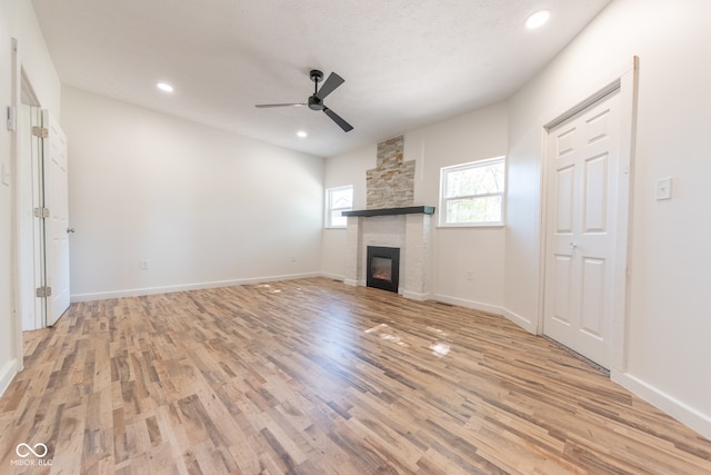 unfurnished living room featuring light wood-type flooring, a textured ceiling, a stone fireplace, and ceiling fan