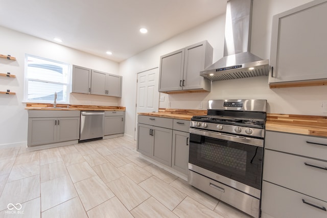 kitchen featuring butcher block countertops, gray cabinets, appliances with stainless steel finishes, and wall chimney range hood