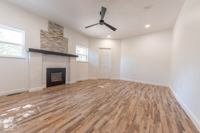 unfurnished living room with light hardwood / wood-style flooring, a large fireplace, and ceiling fan