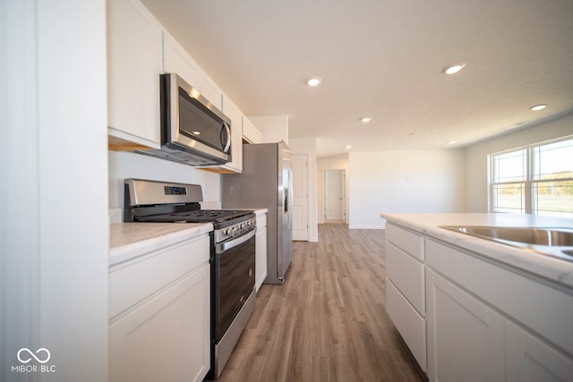 kitchen with stainless steel appliances, light hardwood / wood-style flooring, and white cabinets