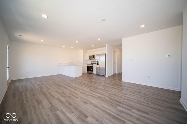 unfurnished living room featuring recessed lighting, a sink, wood finished floors, and baseboards
