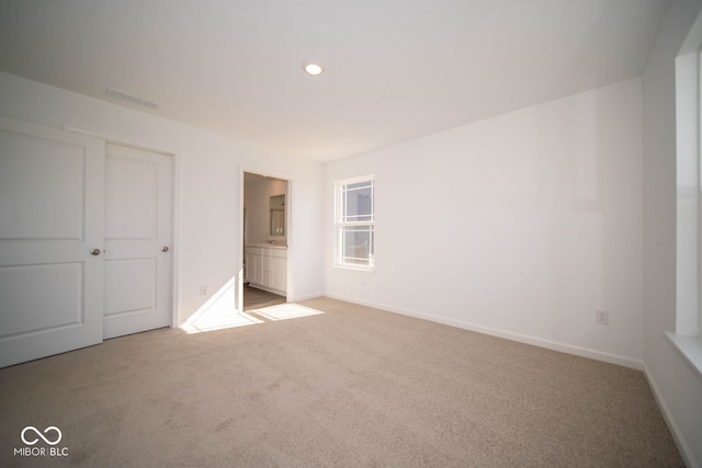 unfurnished bedroom featuring a closet, light carpet, and ensuite bath