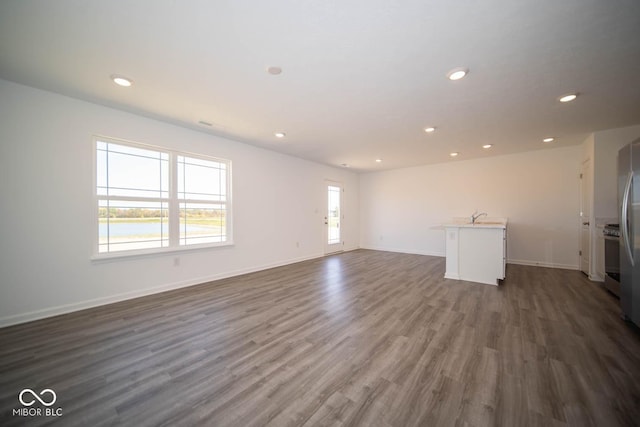 unfurnished living room with recessed lighting, a sink, dark wood-style flooring, and baseboards