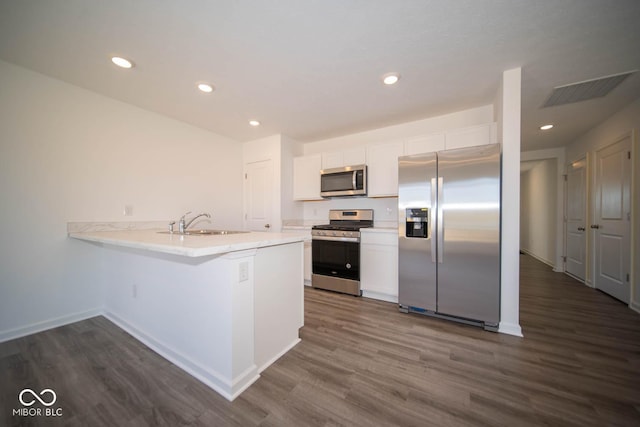 kitchen with white cabinets, stainless steel appliances, light countertops, dark wood-type flooring, and a peninsula