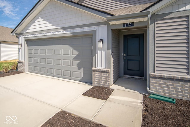 property entrance featuring brick siding, a shingled roof, and concrete driveway