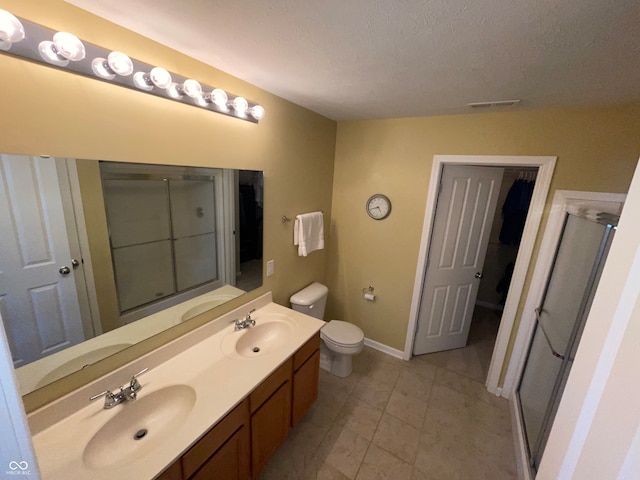 bathroom with toilet, a textured ceiling, vanity, a shower with door, and tile patterned flooring