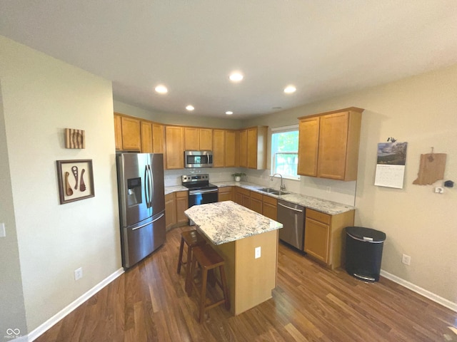 kitchen featuring sink, appliances with stainless steel finishes, a kitchen island, light stone counters, and a kitchen bar