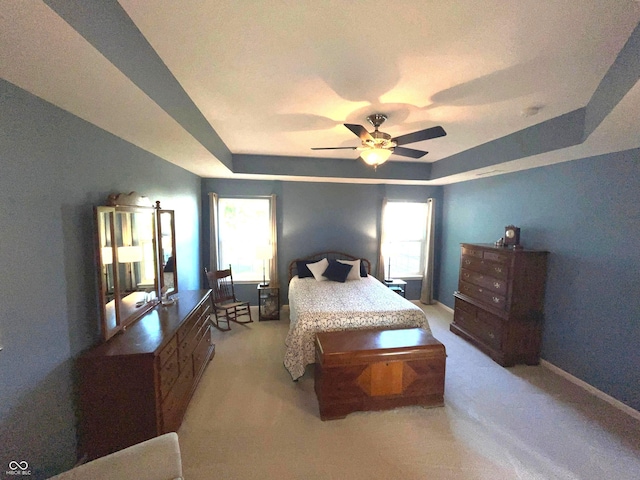 bedroom featuring a raised ceiling, light colored carpet, and multiple windows