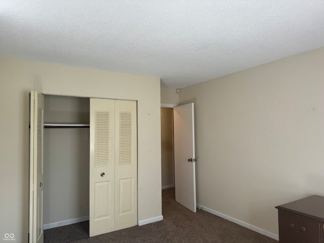 unfurnished bedroom featuring a textured ceiling, dark carpet, and a closet