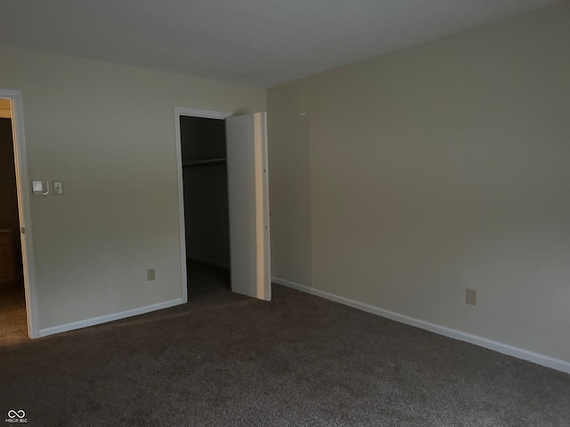 unfurnished bedroom with dark carpet, a walk in closet, and a closet