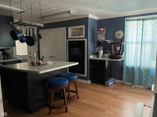 kitchen featuring light hardwood / wood-style floors, ornamental molding, a breakfast bar, and a center island with sink