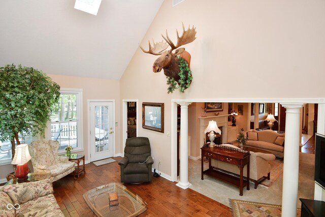 living room with baseboards, ornate columns, a skylight, high vaulted ceiling, and wood-type flooring