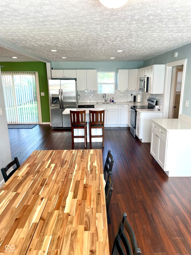 kitchen with appliances with stainless steel finishes, white cabinetry, a center island, and dark wood-type flooring