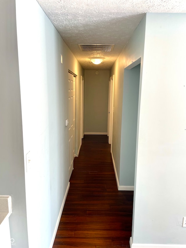 corridor with a textured ceiling and dark hardwood / wood-style floors