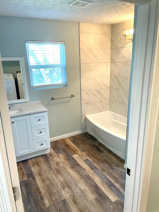 bathroom featuring washing machine and dryer, vanity, a textured ceiling, hardwood / wood-style flooring, and tiled shower / bath