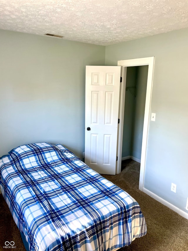 bedroom featuring a textured ceiling, dark carpet, and a closet