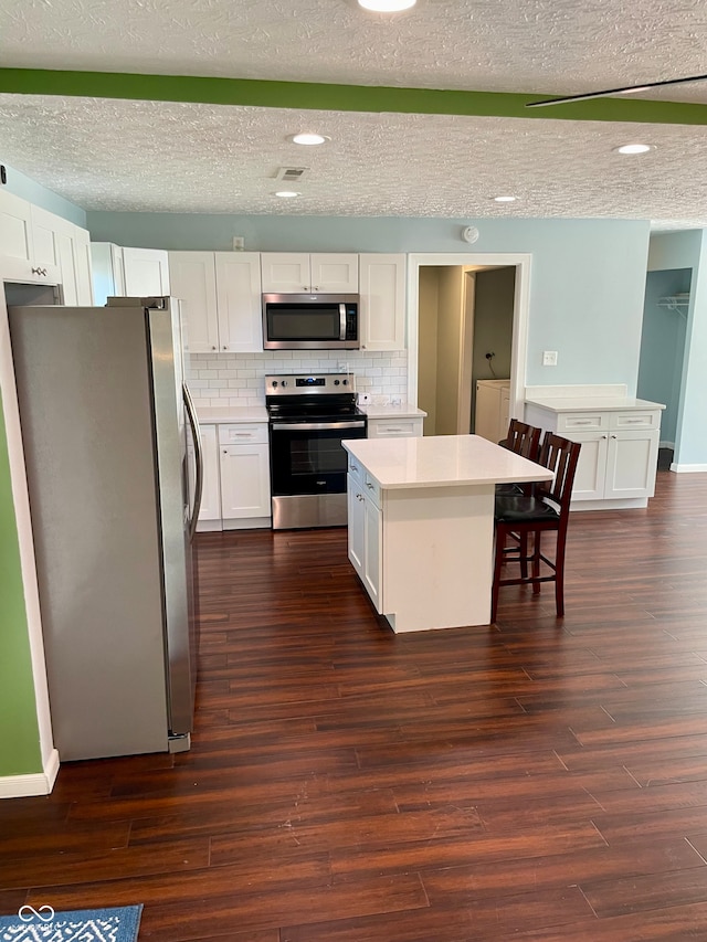 kitchen with dark hardwood / wood-style floors, white cabinetry, a kitchen island, backsplash, and appliances with stainless steel finishes