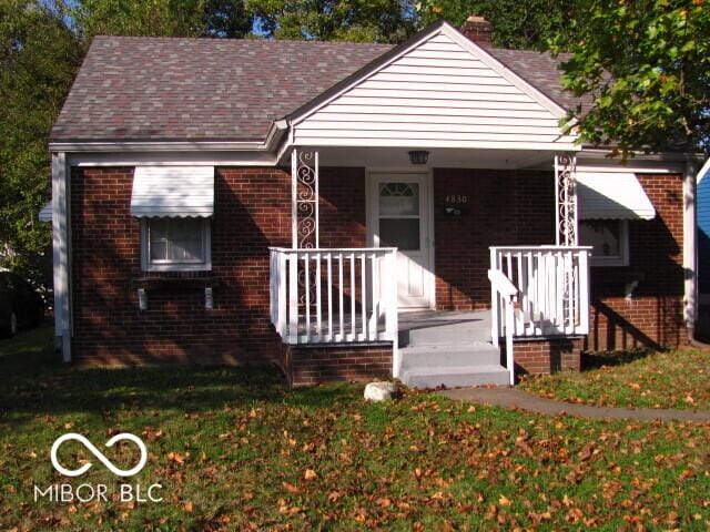 bungalow featuring a front yard, covered porch, brick siding, and roof with shingles