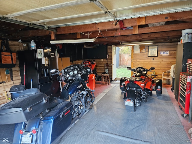 garage with wood walls and black refrigerator with ice dispenser