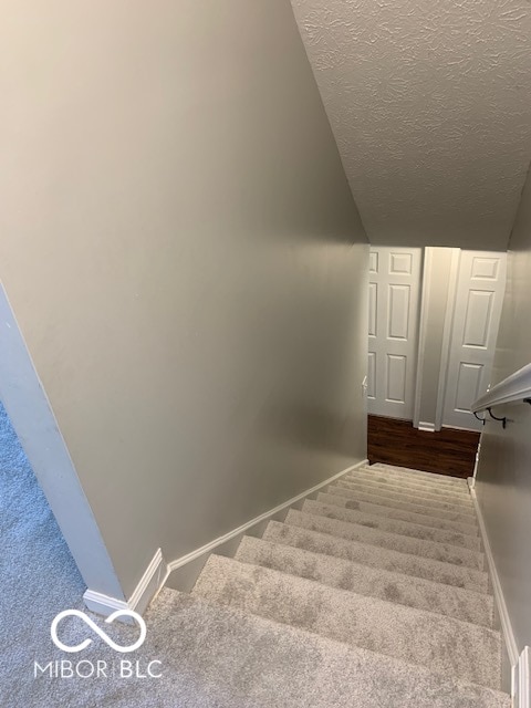 stairway with carpet floors, vaulted ceiling, and a textured ceiling