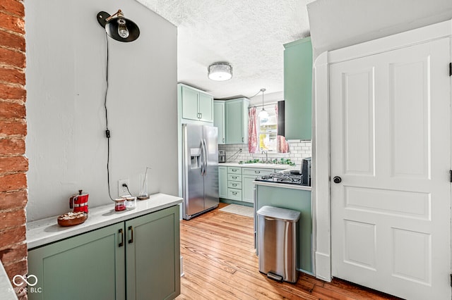 kitchen with stainless steel fridge, backsplash, green cabinetry, a textured ceiling, and light hardwood / wood-style flooring